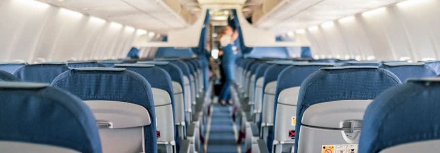 Empty airplane seats with a flight attendant standing in the aisle.